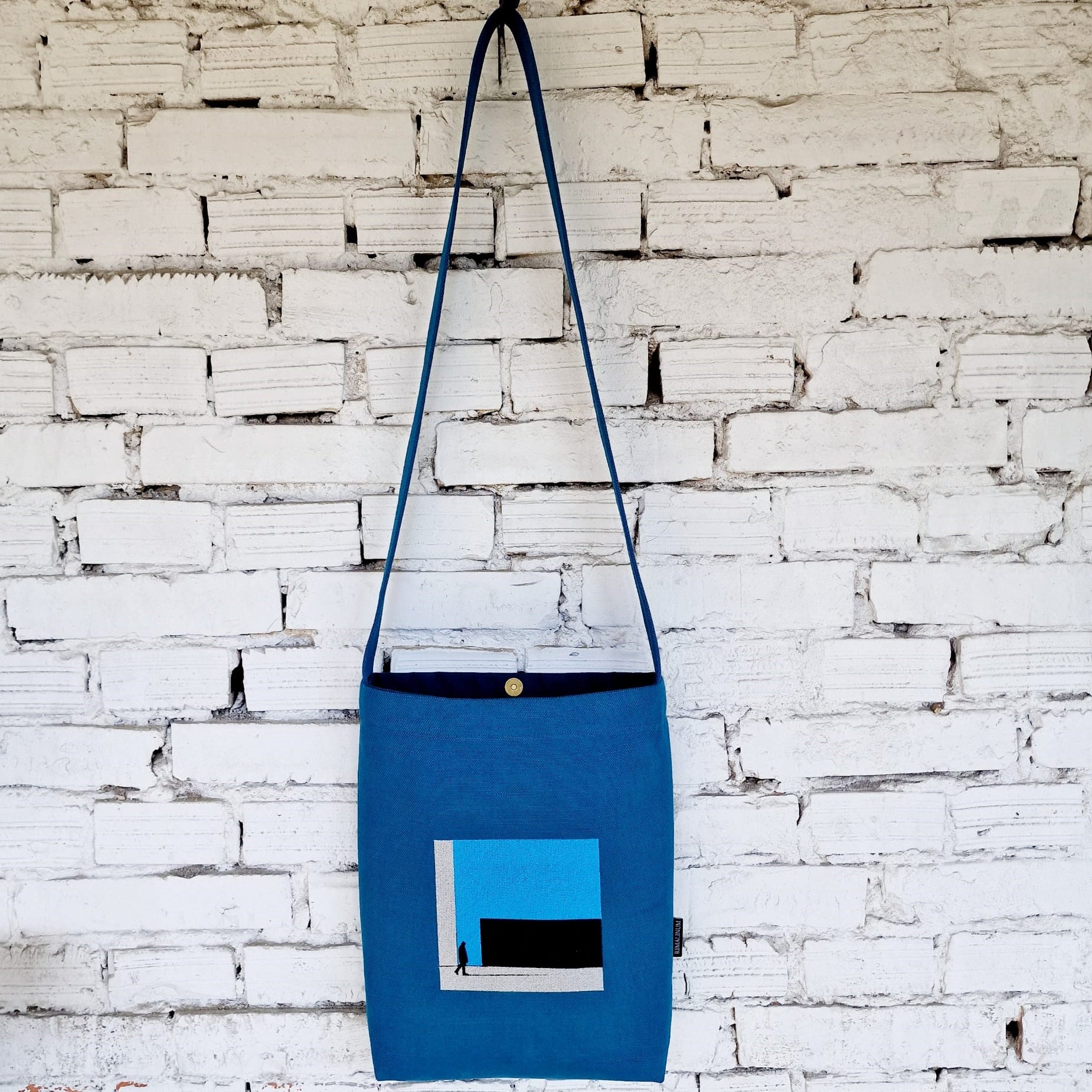 Handmade blue linen and cotton canvas crossbody bag hanging on a white brick wall