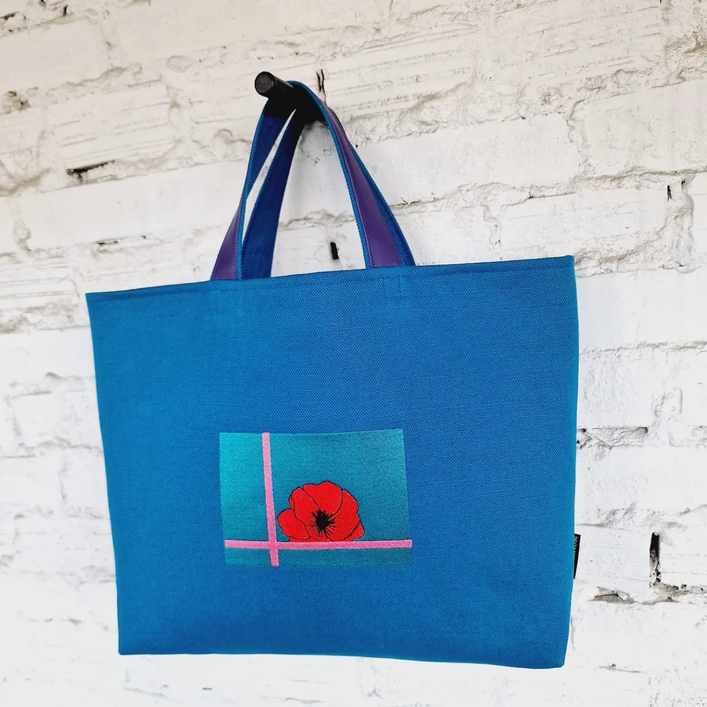 Blue linen and cotton canvas handbag with purple leather-reinforced handles and modern red poppy embroidery