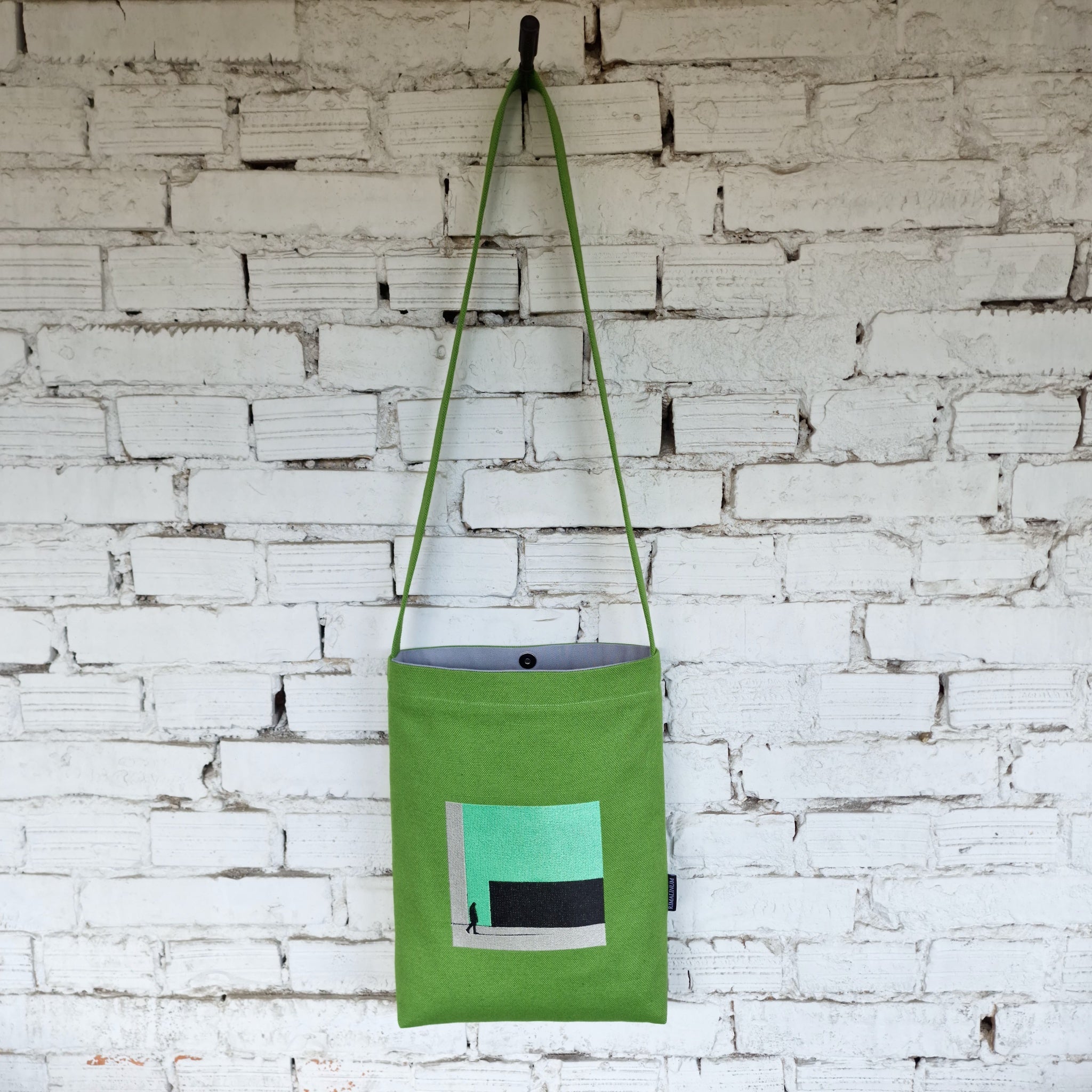 Full view of green linen and cotton crossbody bag with long strap, minimalist embroidery, and snap button closure