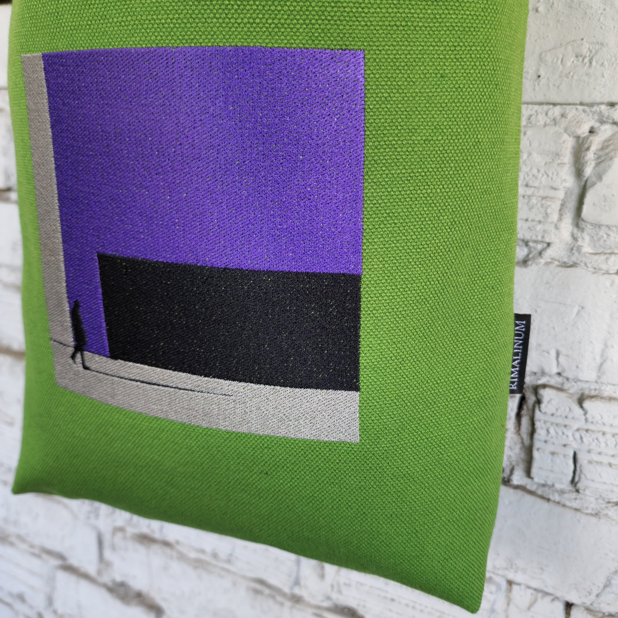 Close-up of urban-inspired embroidery on green canvas crossbody bag, featuring modern purple and black design and Rimalinum logo